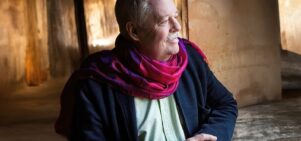 Image of Armistead Maupin looking to thier side, wearing a navy blue cardigan and magenta scarf