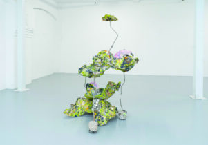 A free standing sculpture of greens, blues, purples and greys with wire.