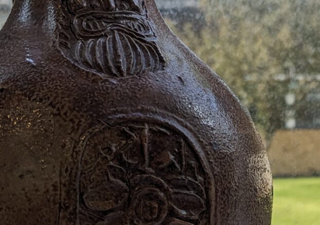 An earthern ware jar with a face and pattern on.