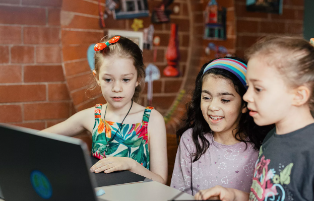 Three children look at a laptop screen.