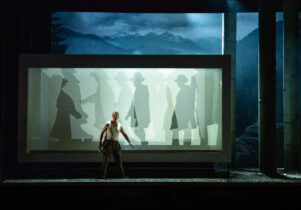 Blond Eckbert production image. Man on stage with screen behind him showing shadow figures.