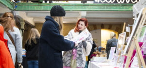 A smiling market trader shows a customer a painting in Victoria Baths