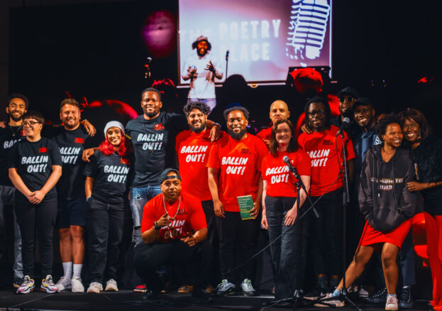 The Poetry Place team stand on stage in red and black T shirts reading ' Ballin Out'.