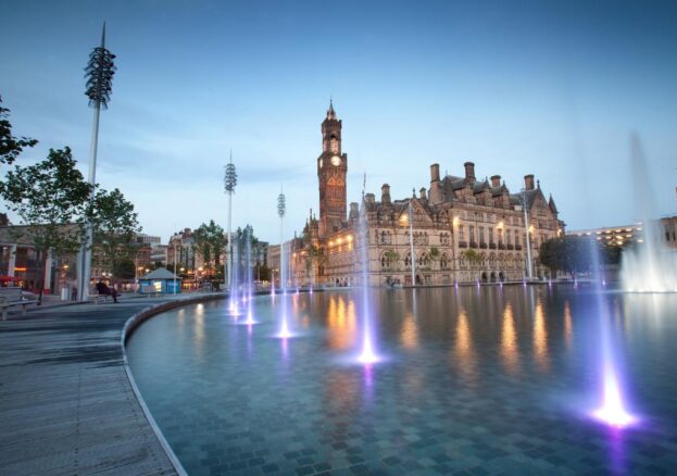 Get Outside with Bradford 2025: An image of a large man made pool with fountains in front of a historic building with a clock tower