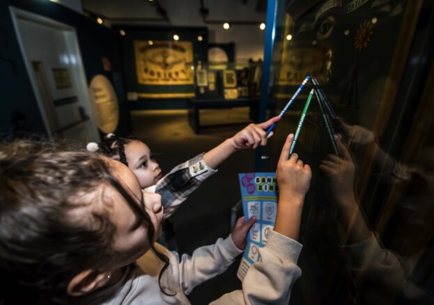 Two young visitors looking up at a banner in a case, holding pencils and an activity sheet.