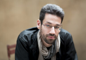 Male with beard and glasses sitting on chair with leather jacket