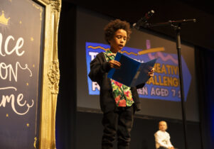 Creative writing challenge prize giving, a young boy on stage reading in front of a microphone Creative Writing Challenge at the lowry