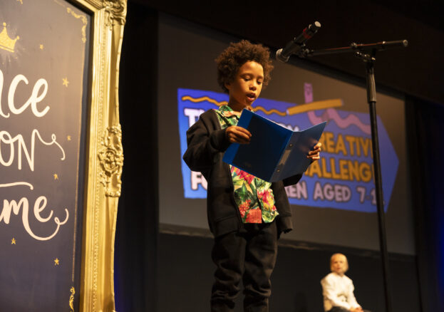 Creative writing challenge prize giving, a young boy on stage reading in front of a microphone Creative Writing Challenge at the lowry