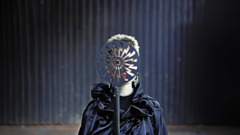 A person wearing black stands behind a circular object with lightning bolt cut outs