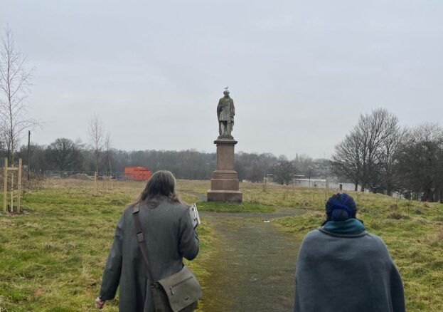 Heritage walkers on Monument Moor in Leeds, walking towards the statue of Henry Rowland Marsden. A seagull is sitting on the statue's head.
