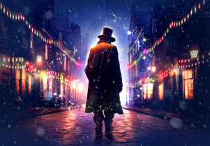 A Christmas Carol at Octagon Theatre Bolton. A person in a long coat and top hat walks alone down a cobblestone street at night, surrounded by colorful holiday lights and softly falling snow. The scene glows warmly from shop windows and string lights, creating a festive and mysterious atmosphere.
