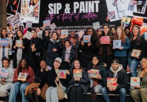 Crowd of people holding up their newly created artworks in front of a sign for Sip and Paint.