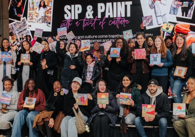 Crowd of people holding up their newly created artworks in front of a sign for Sip and Paint.