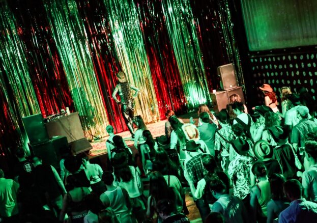 Group of people line dancing, following the steps of a single person on stage with a glittery backdrop.