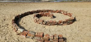 a beach. red bricks are laid out in a spiral shape on the sand.