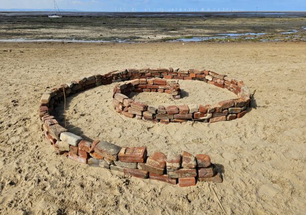 a beach. red bricks are laid out in a spiral shape on the sand.